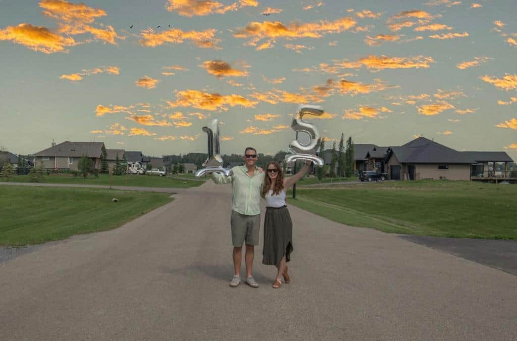 Rainbow Williams and Sarah Corker holding up decorative 15th anniversary balloons at Spring Lake Ranch with clouds lit red by the sunset in the background